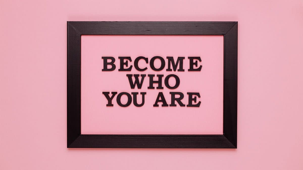 Inspiring quote 'Become Who You Are' framed on a vibrant pink wall, perfect for encouragement.
