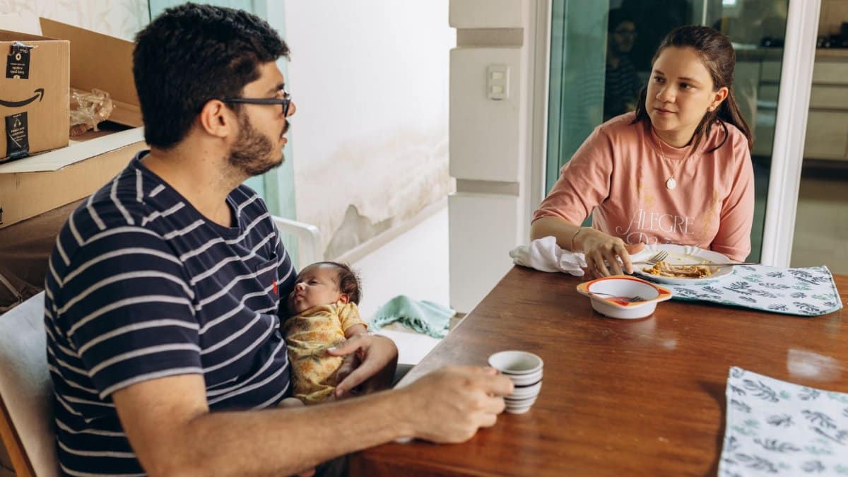 A young couple enjoys a meal at home with their baby sitting at the dining table.