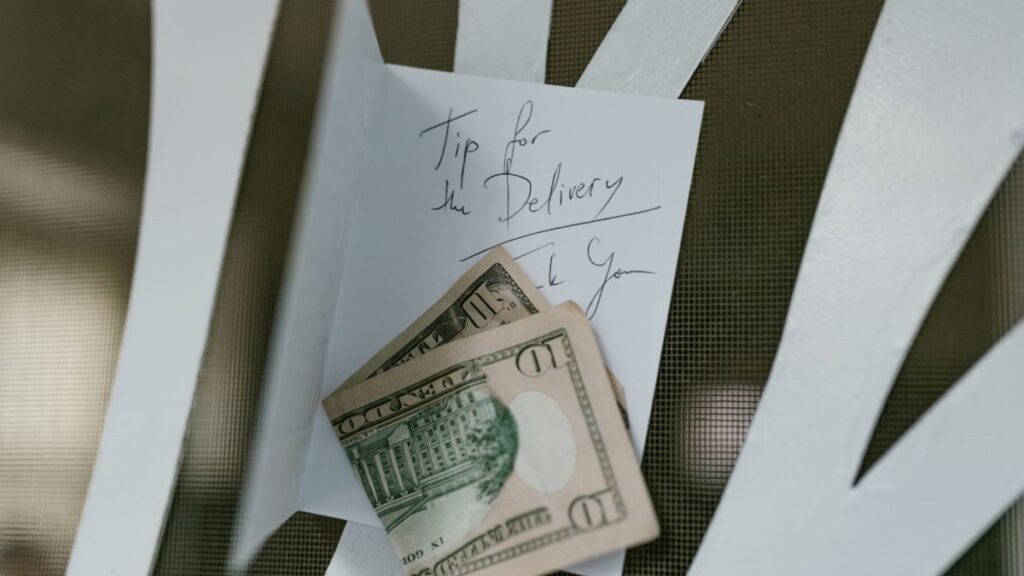 A photo of US dollar bills placed with a handwritten tip note for delivery service.
