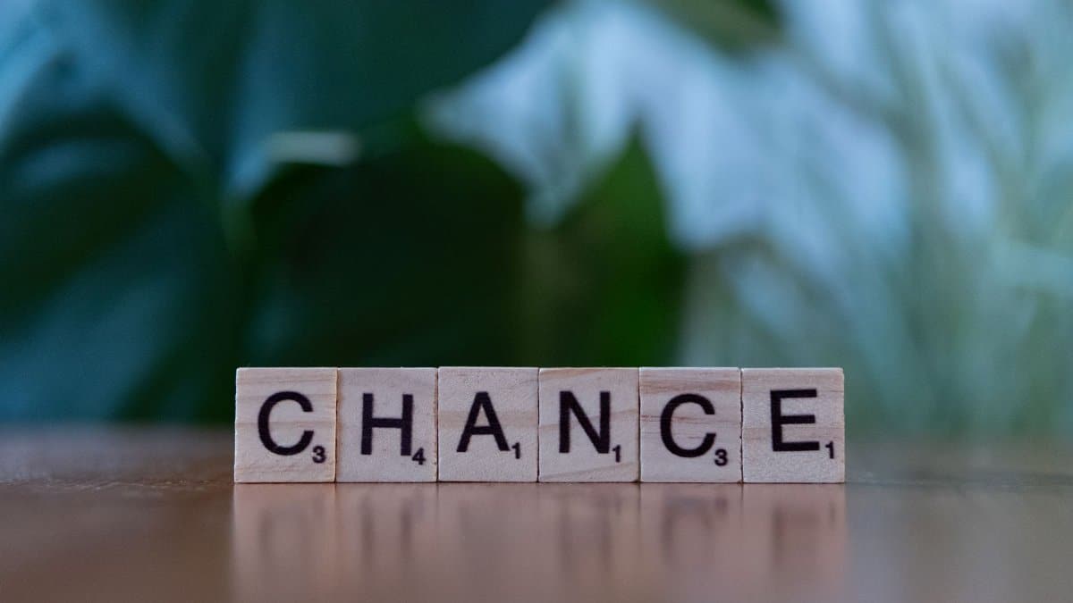 Scrabble tiles spelling 'chance' on a wooden surface with a blurred green background.