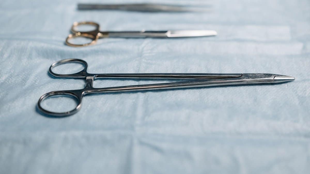 Close-up of surgical tools including a needle holder on a blue cloth in a medical setting.
