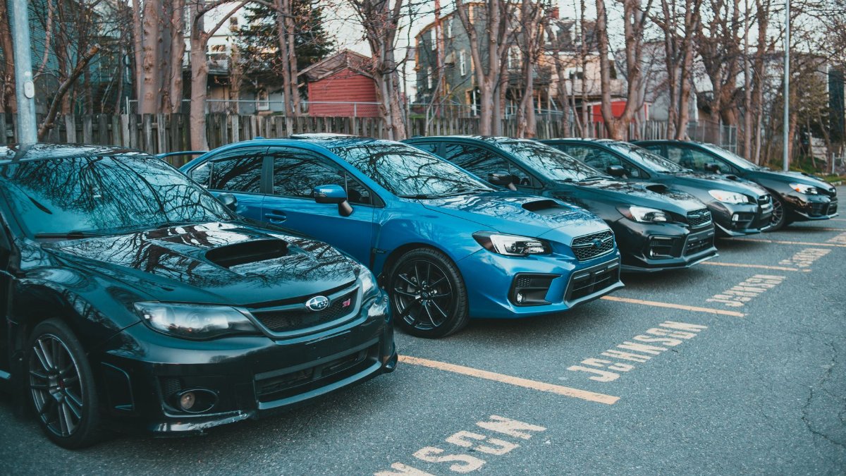 Multiple Subaru cars parked in an outdoor lot lined with trees, showcasing automotive design.
