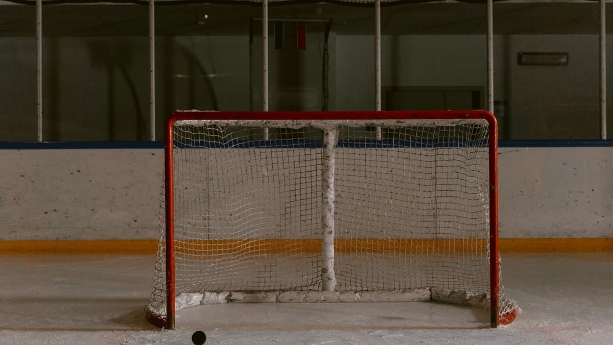 A still shot of an ice hockey rink featuring an empty goal net and puck on the ice.
