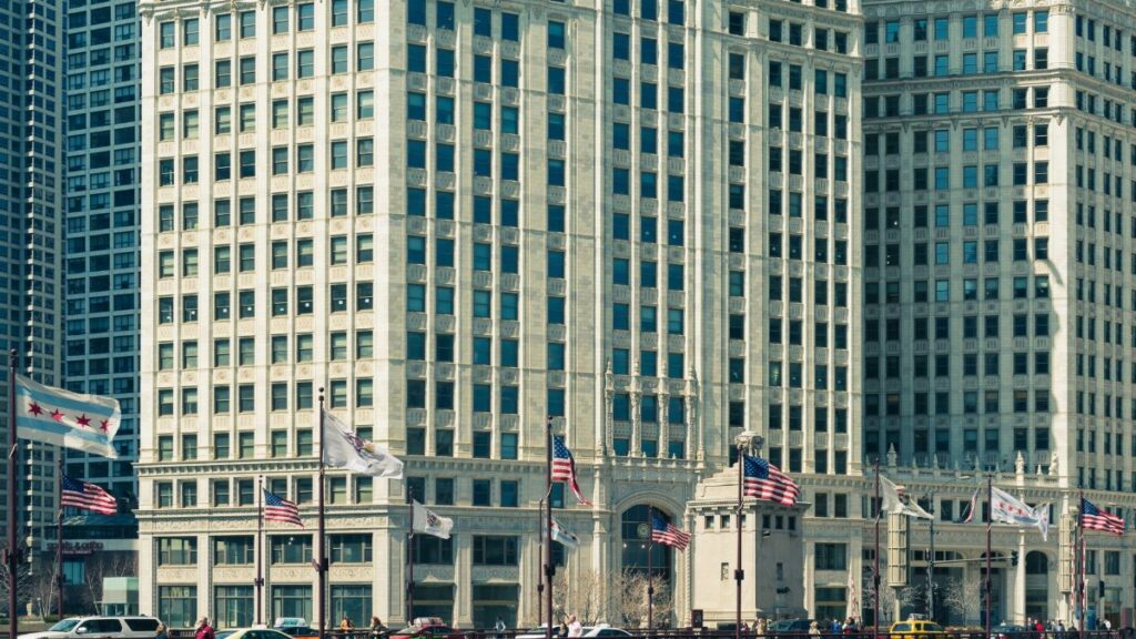 Street view of Chicago skyscrapers adorned with American and city flags on a sunny day.