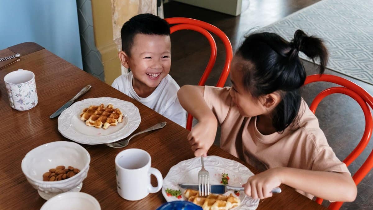 Smiling children having waffles and enjoying breakfast indoors.