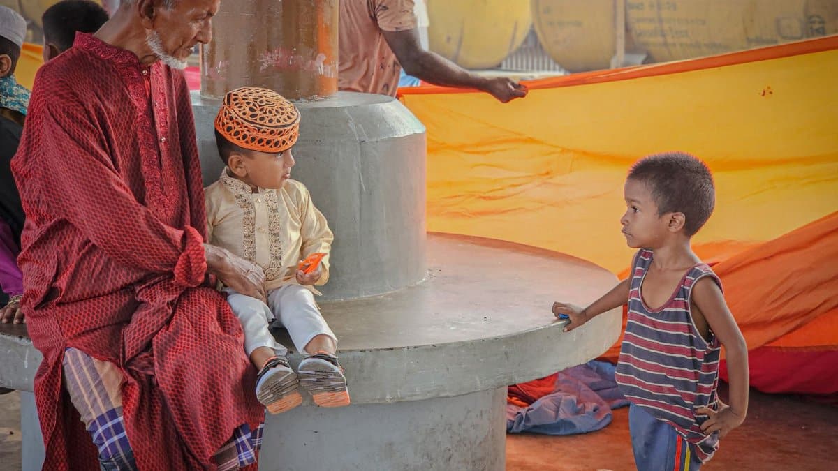 A senior man with children interacts in a vibrant outdoor environment, highlighting cultural attire and vibrant colors.
