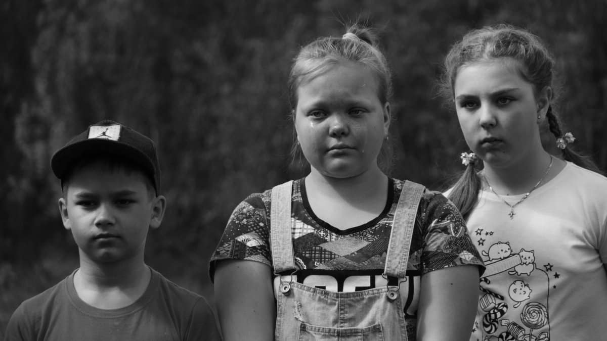 A black and white photo capturing three children standing outdoors, showing serious expressions.