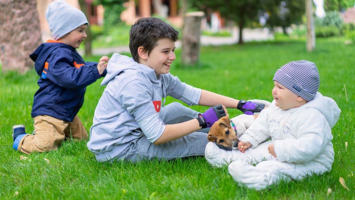 Three children enjoy a day outdoors, playing with a small puppy on a vibrant green lawn.