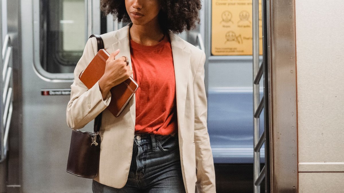 Confident woman in a blazer with notebook and purse walking in a subway train.