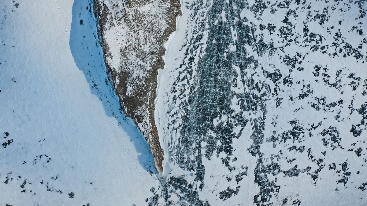 Aerial view of rocky formation on icy sea with snow and shadow in wintertime on sunny day
