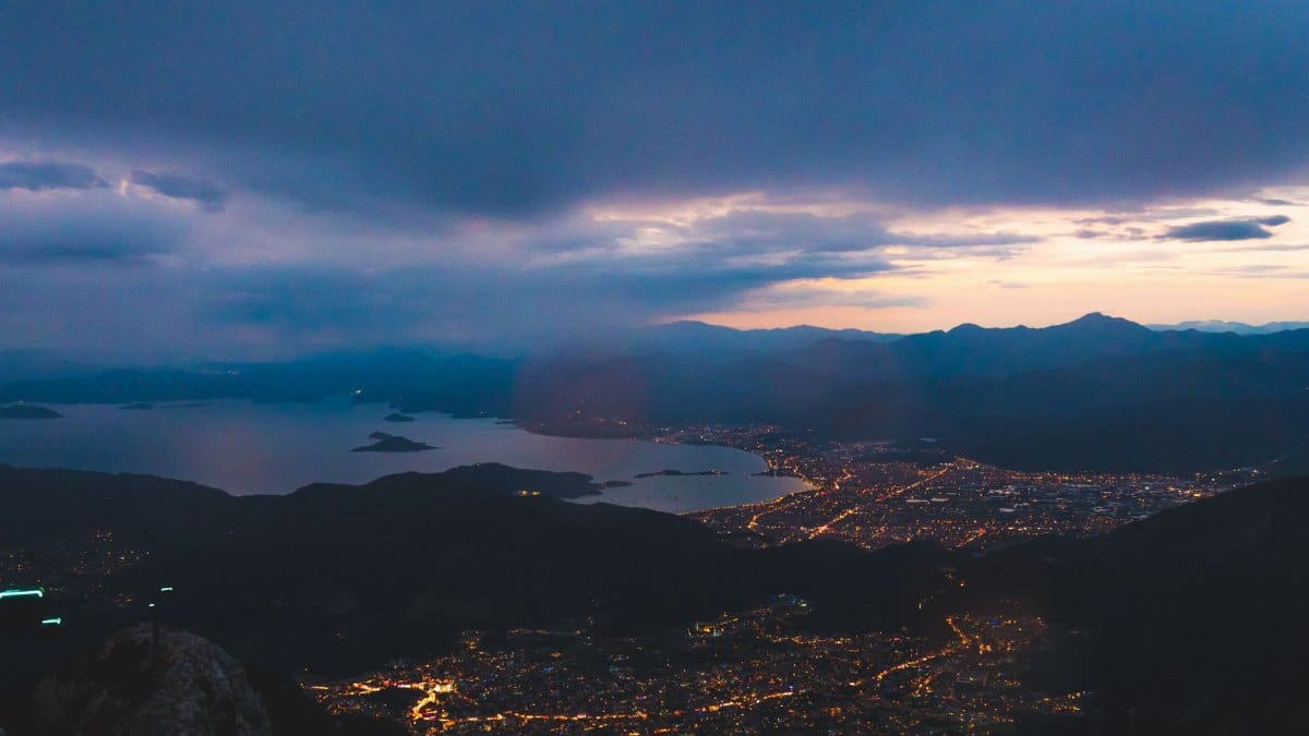 Elegant aerial view of city lights beneath a cloudy twilight sky over a coastal landscape.