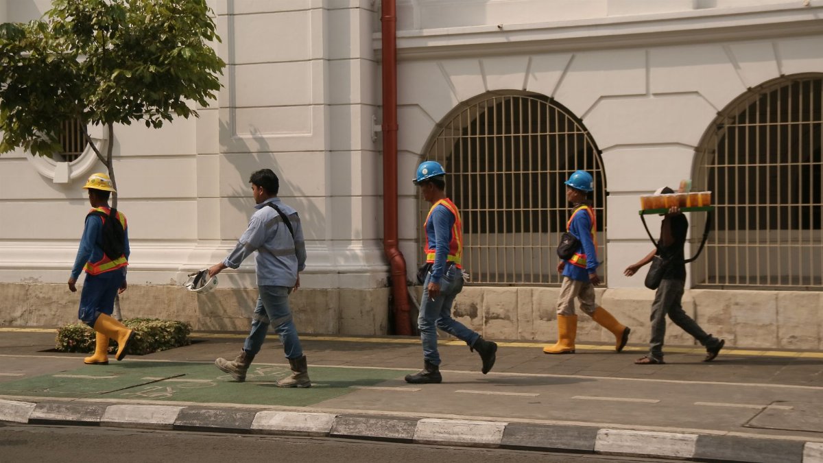 Group of construction workers walking along a city street under clear daylight conditions.