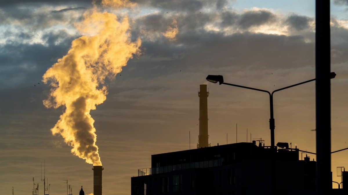 Silhouette of a factory chimney emitting smoke against a sunset sky, highlighting air pollution.