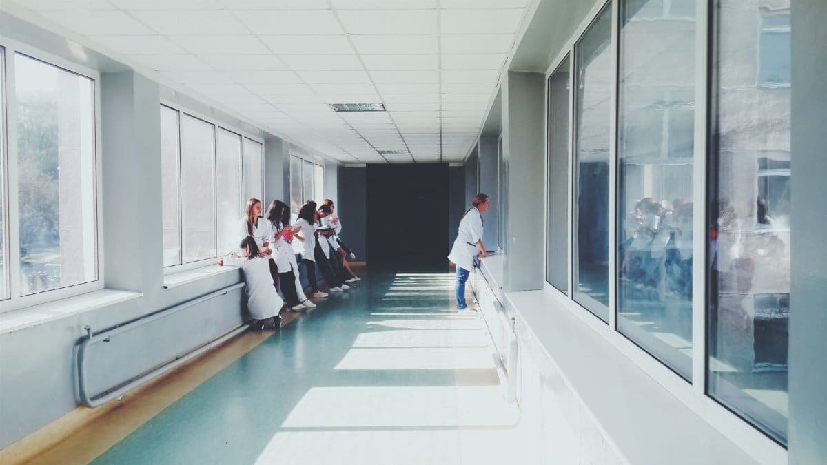A brightly lit hospital hallway with medical staff in white coats, conveying a professional healthcare environment.