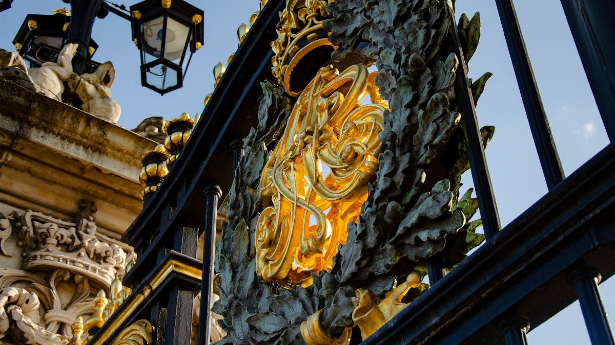 Close-up of gilded ironwork at Buckingham Palace gates in London, showcasing intricate design.
