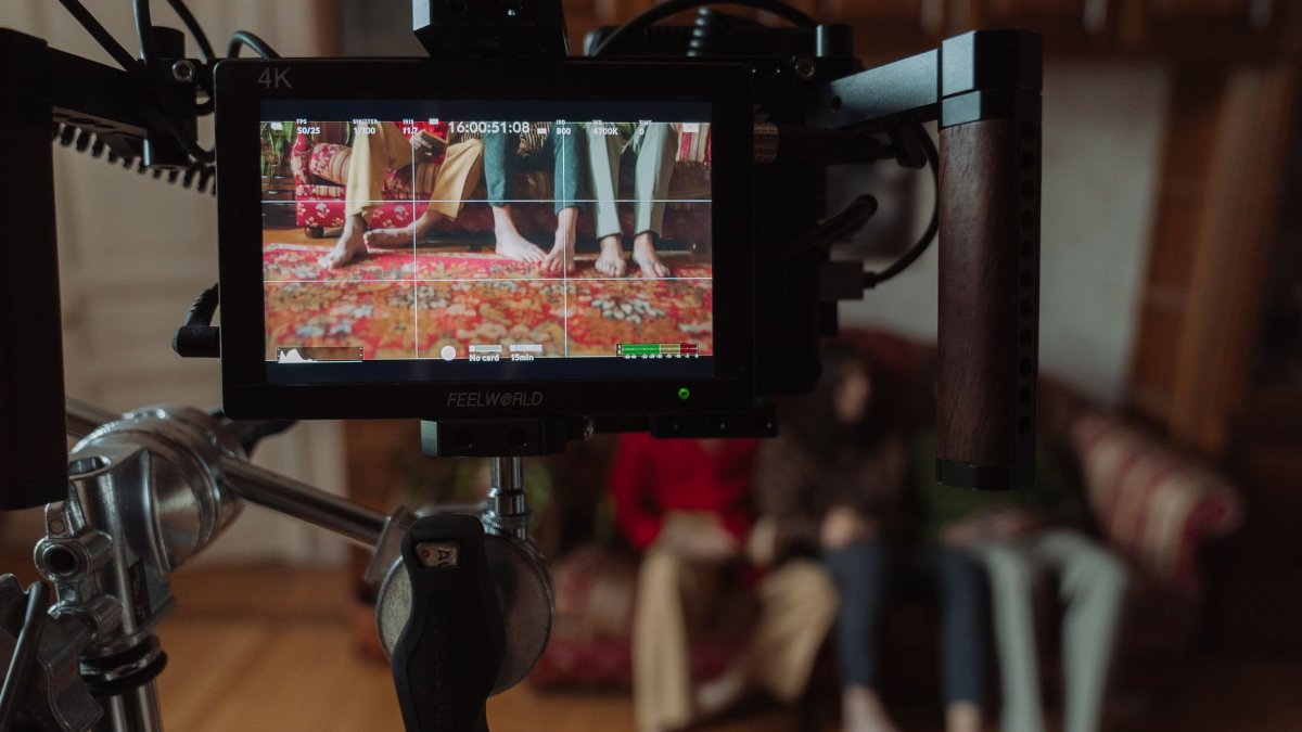 Film set monitor showing a scene with barefoot people sitting on a couch captured during production.