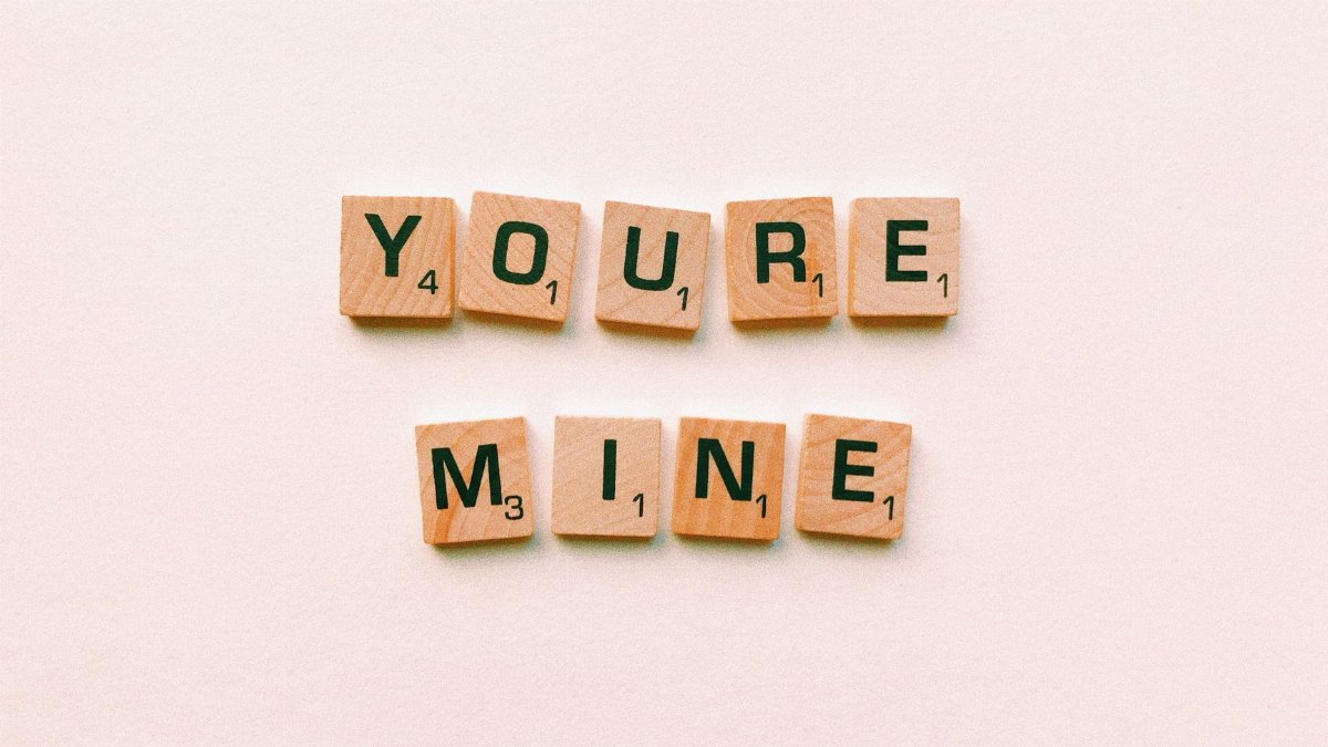Romantic message You're Mine created with wooden Scrabble tiles on a pink background.