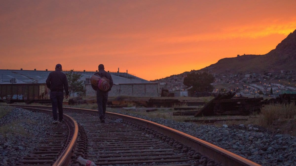 Two men walking along railway tracks during a stunning sunset in Chihuahua, Mexico.