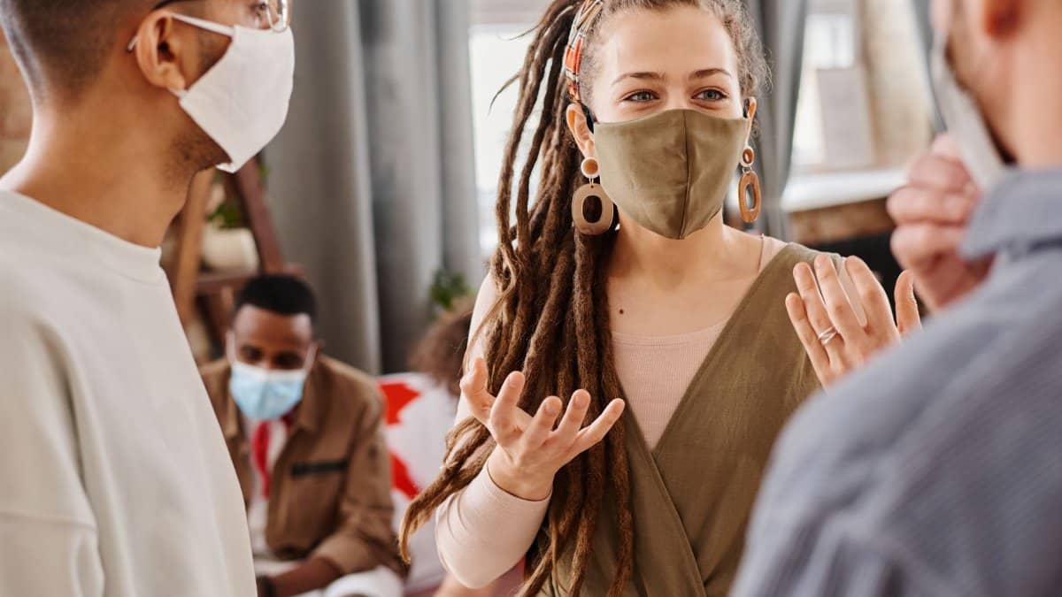 A group of diverse adults communicating indoors while wearing face masks.