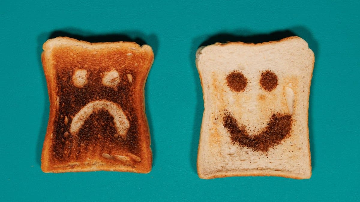 Two slices of toast with happy and sad faces on a teal background.