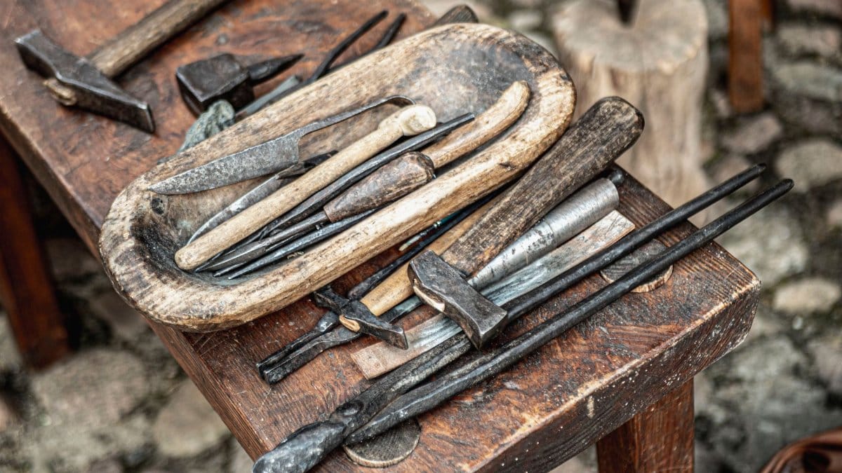 A collection of vintage blacksmith tools displayed on a wooden table outdoors.