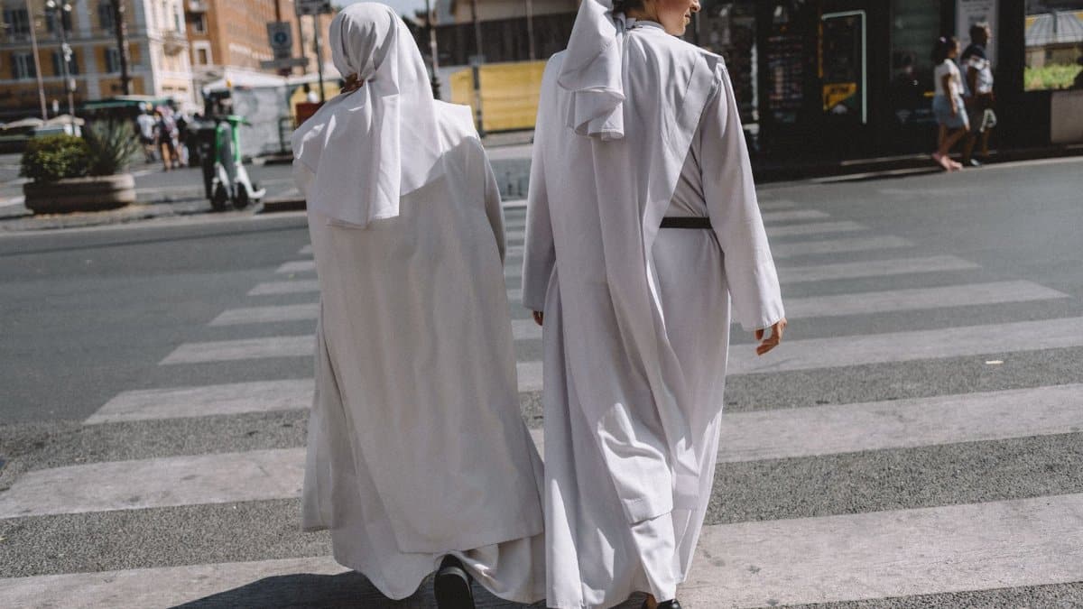 Two nuns in white habits cross a street in Vatican City, showcasing urban spirituality.