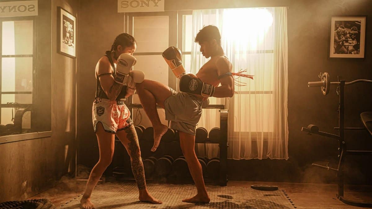 A male and female athlete engage in a dynamic Muay Thai sparring session.