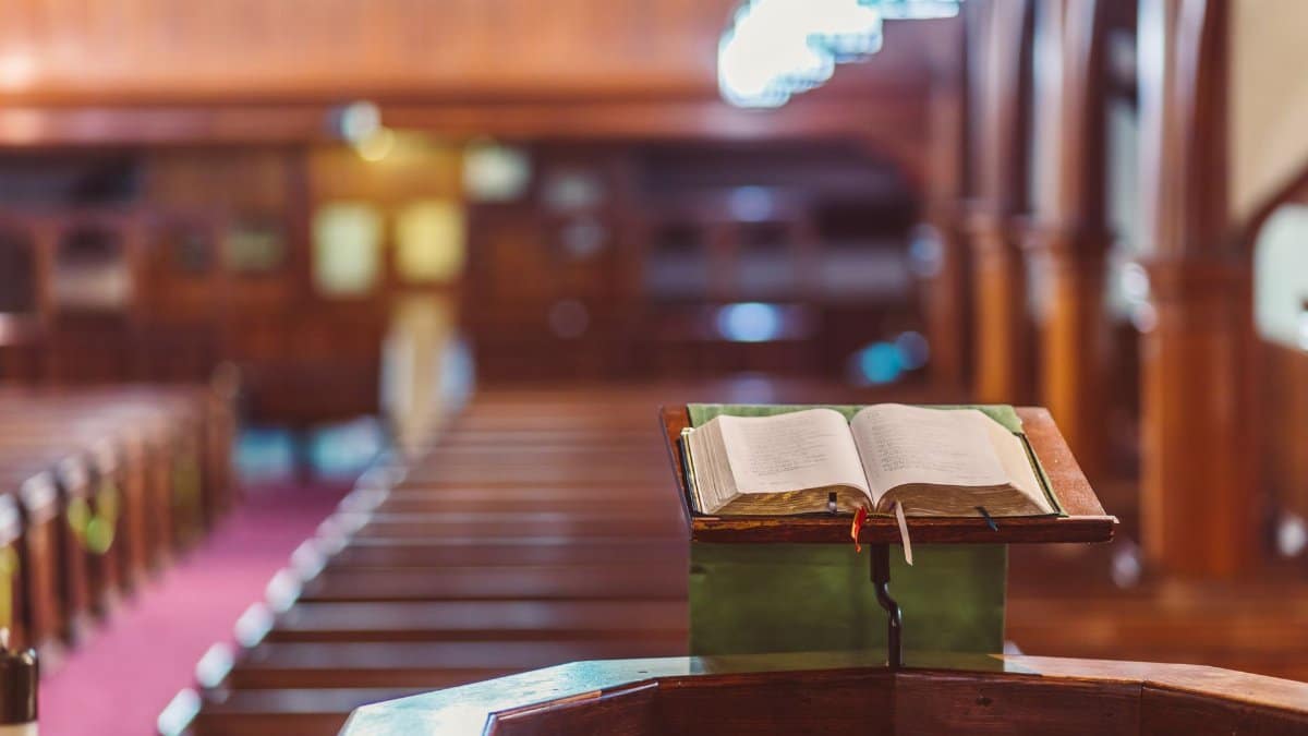 Open Bible on a wooden pulpit in a serene church setting with blurred pews in the background.