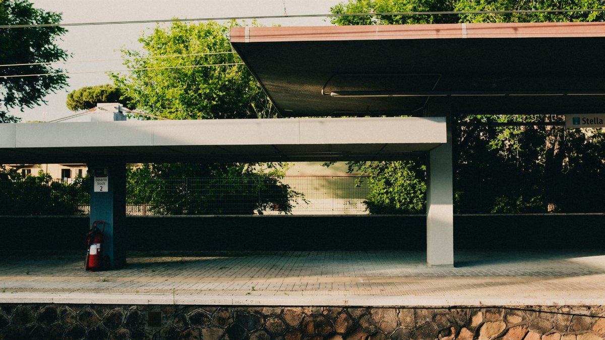 Quiet and empty railway platform with trees in Italy, emphasizing urban travel aesthetics.