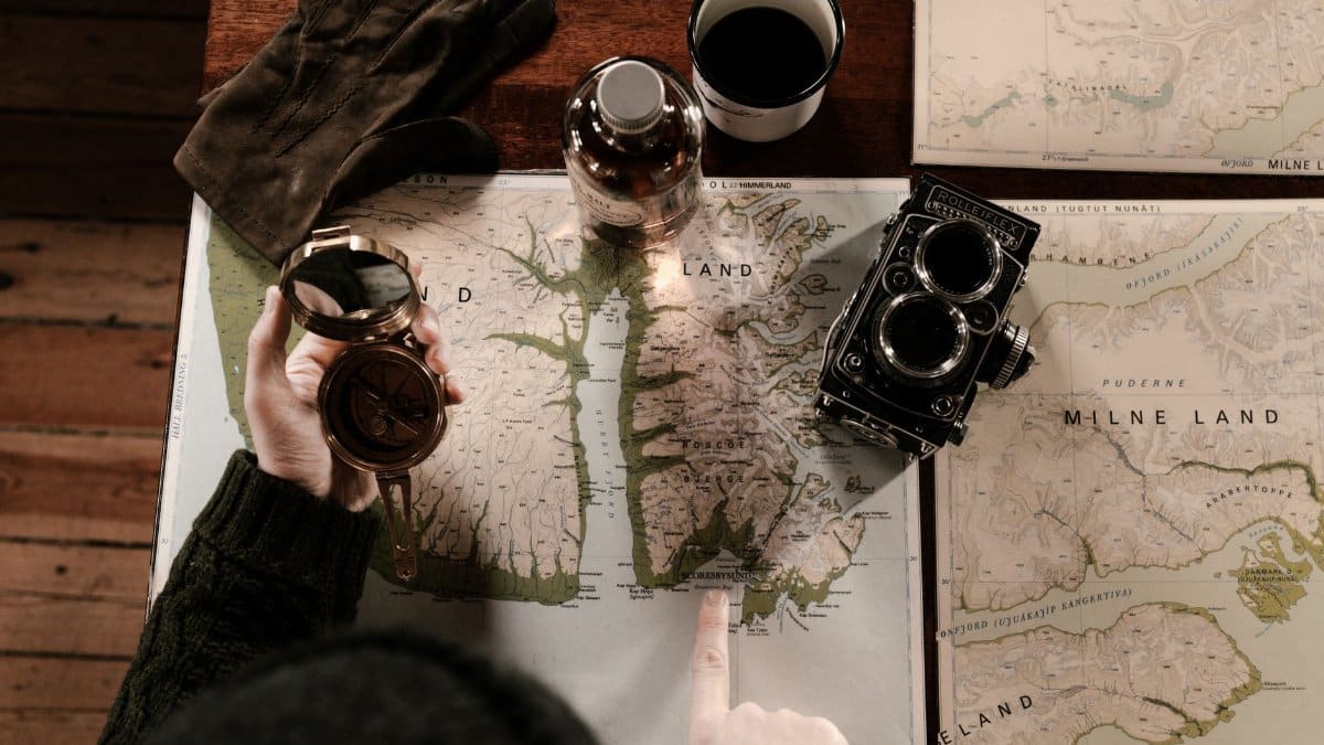 Top view of vintage exploration setup with maps, compass, gloves, and retro camera.