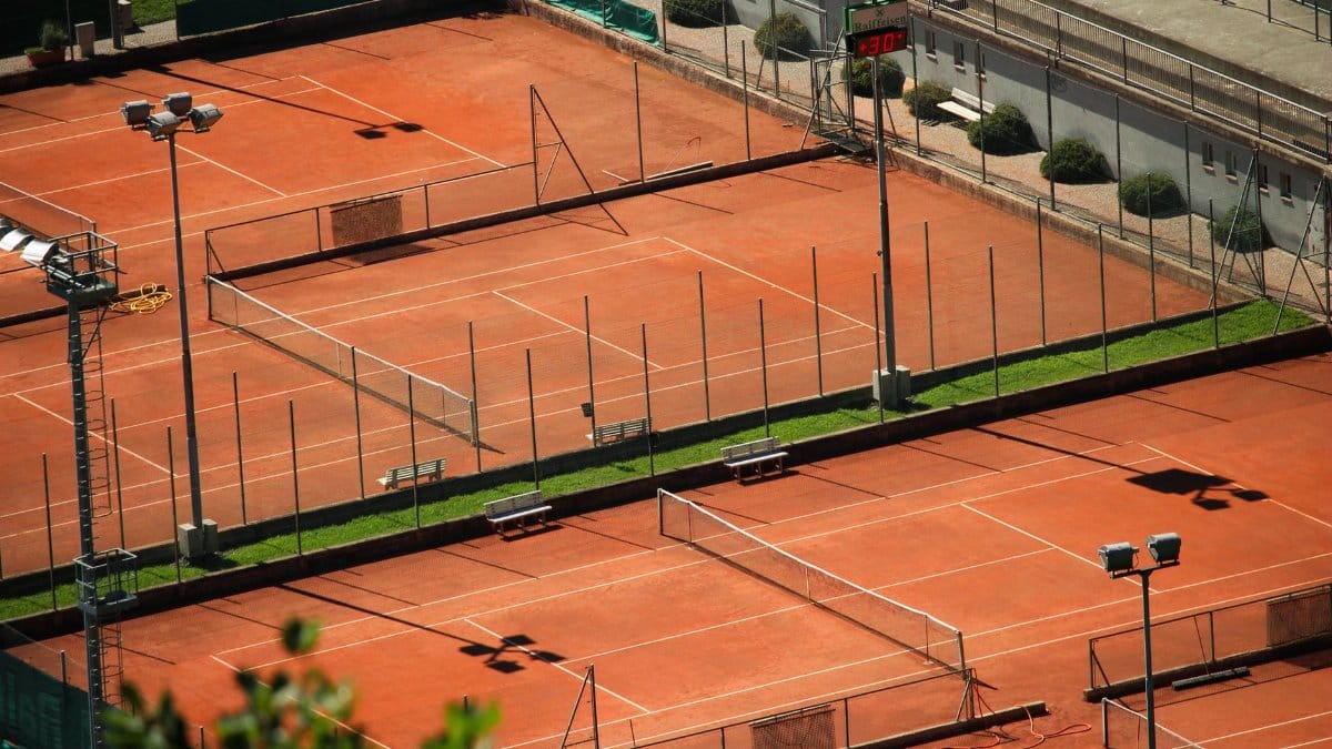 Aerial shot of empty red clay tennis courts on a sunny day with shadows.