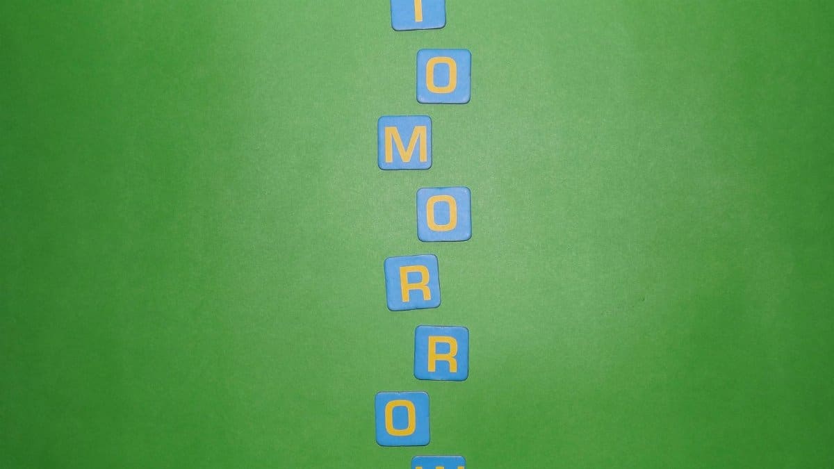 Vertical arrangement of blue letter tiles spelling 'TOMORROW' on a green background.