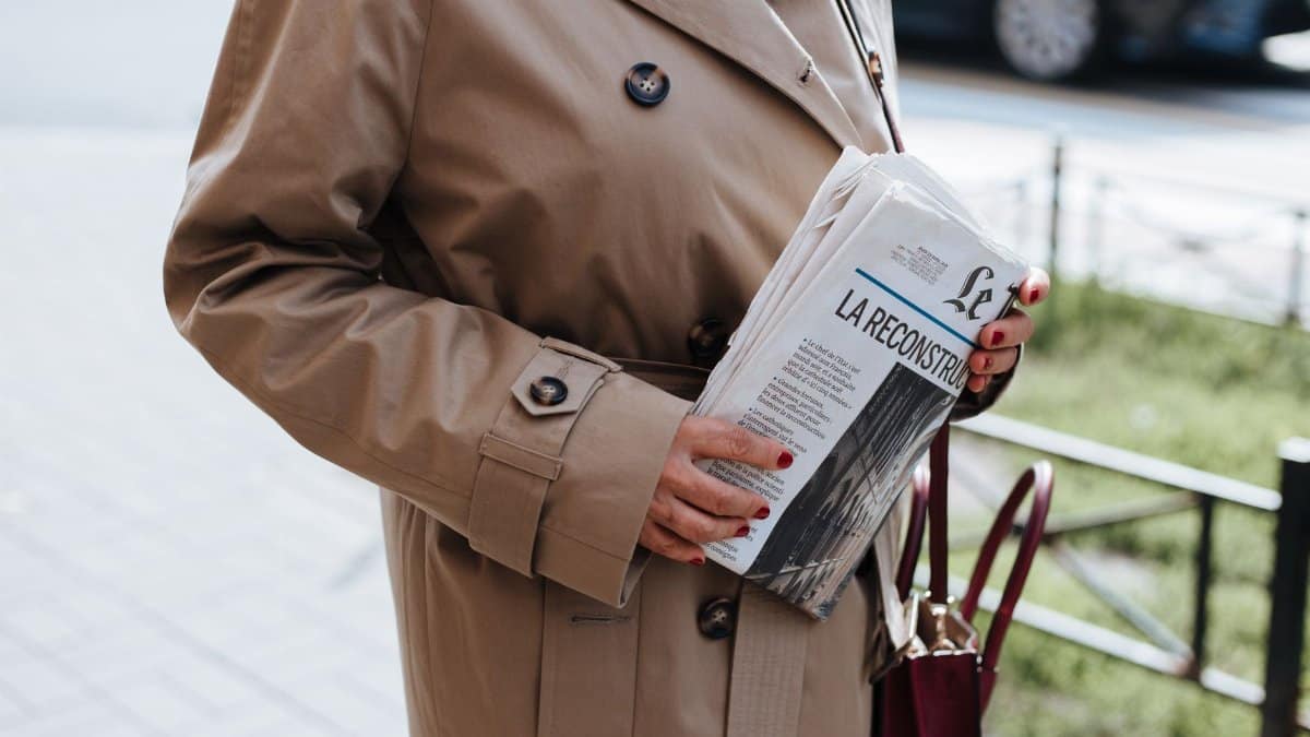 Fashionable woman in trench coat with newspaper and manicured nails on a day walk.