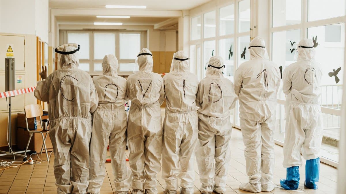 Healthcare professionals in PPE suits with COVID-19 text, back view, indoors.
