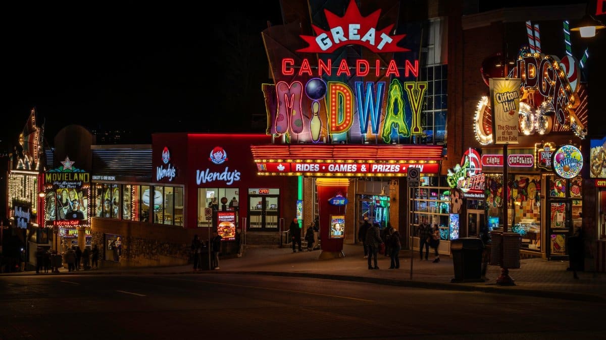 Colorful neon-lit street scene at night featuring the Great Canadian Midway.