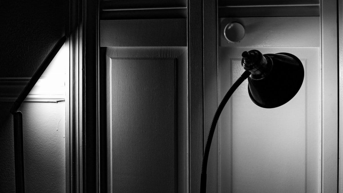 Elegant black and white shot of a room with a focused lamp casting dramatic shadows on the walls.