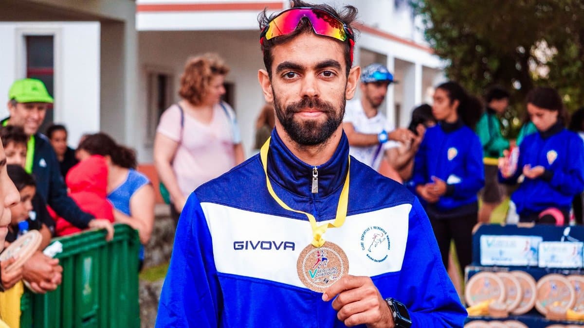 A bearded man proudly displays his medal at an outdoor sporting event surrounded by people.