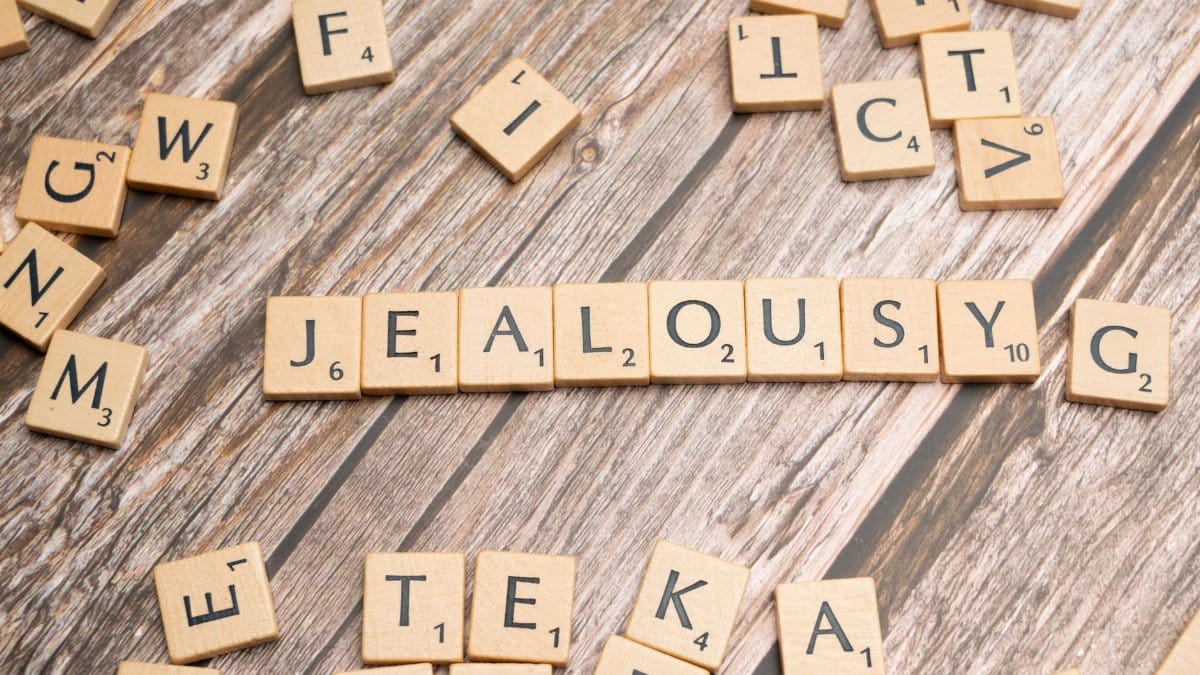 Wooden Scrabble letter tiles forming the word 'Jealousy' on a rustic wooden surface.