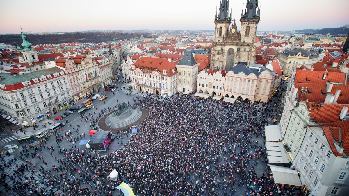 Drone view of crowd of people standing on square near gothic aged church and old town hall located in Prague