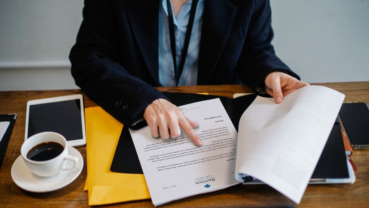 High angle of crop faceless woman in formal wear sitting at wooden table with tablet and coffee and reading documents