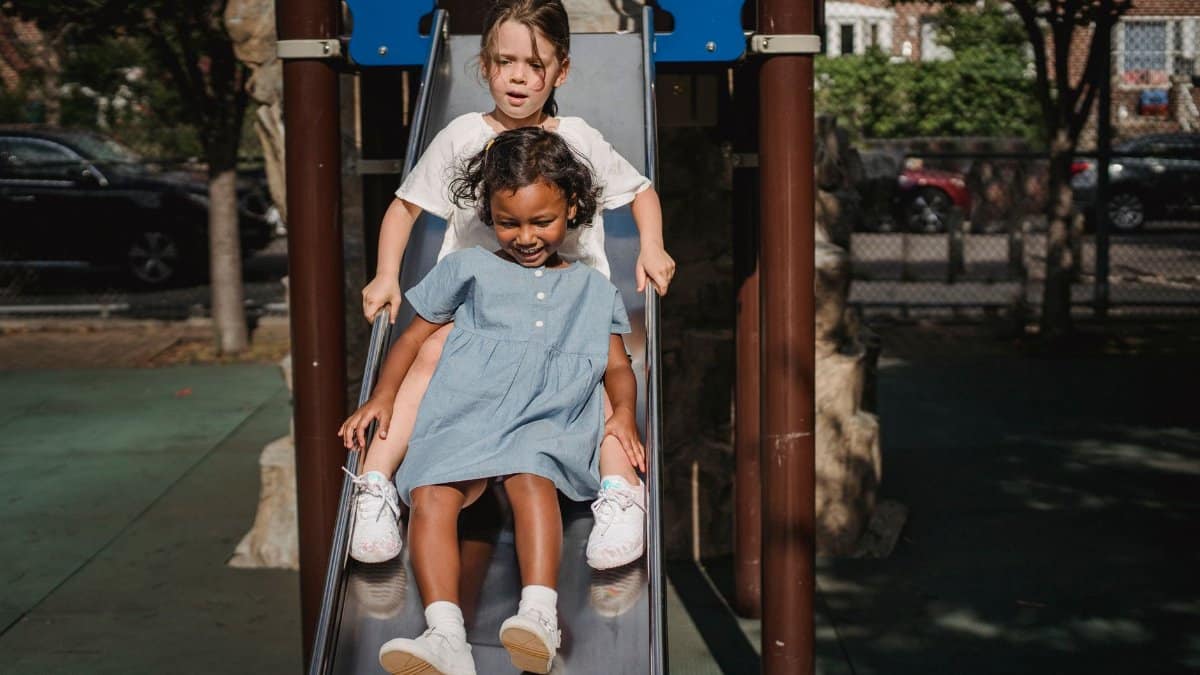 Two children enjoying a slide on a sunny day at an outdoor playground, experiencing fun and excitement.