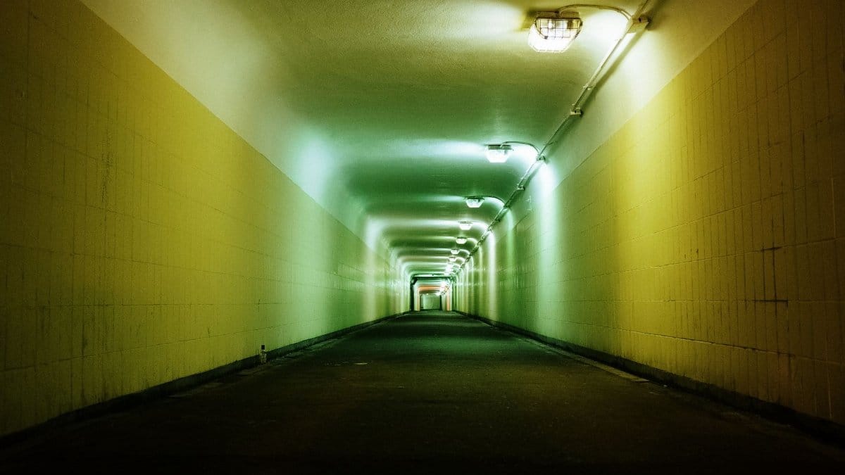 A long urban tunnel illuminated by green and orange lights, showcasing symmetry and an empty atmosphere.