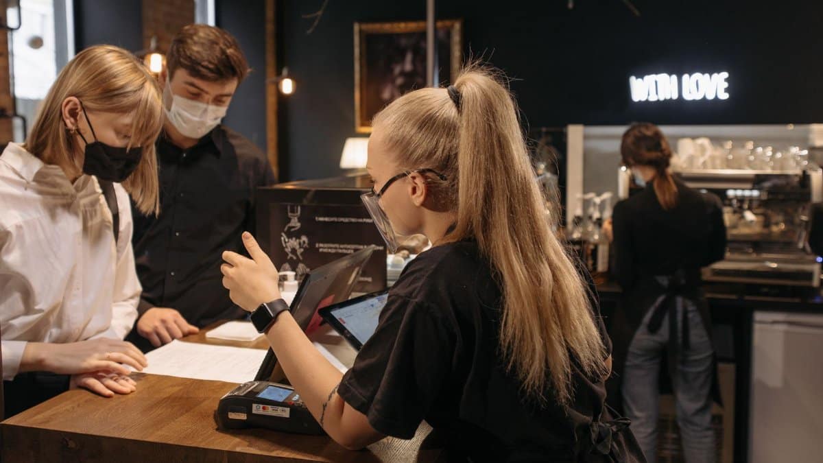 Barista attending to customers in a café using contactless payment during pandemic.