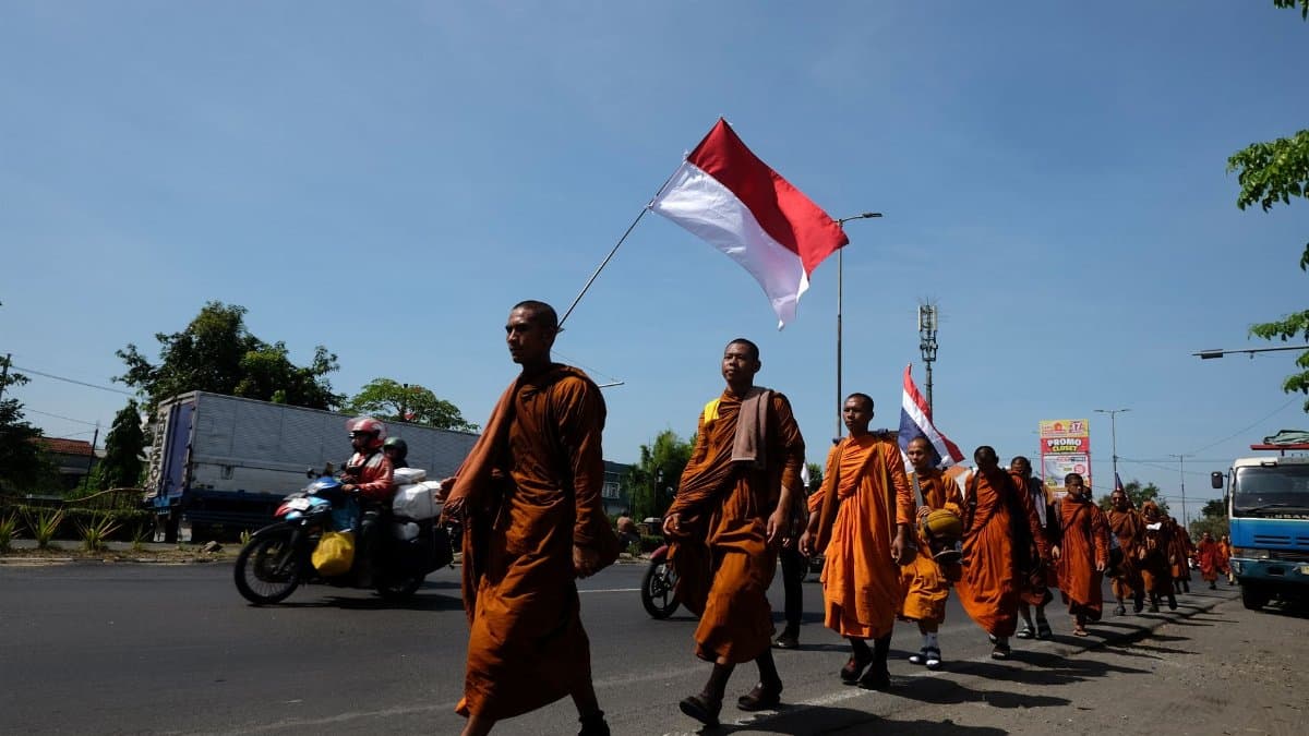 A group of Buddhist monks in orange robes march carrying the Indonesian flag on a street during the day.
