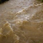 A muddy river flowing rapidly through a natural landscape after heavy rain, showcasing erosion and flooding.
