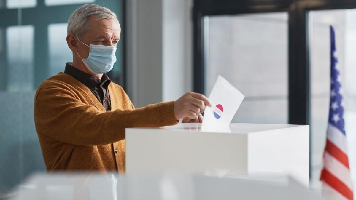 An elderly man wearing a face mask votes in-person, highlighting safety during the pandemic.