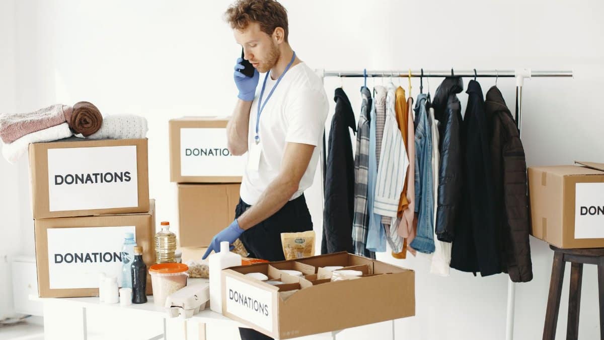 A volunteer organizes donation boxes and clothes while making a phone call in a bright room.