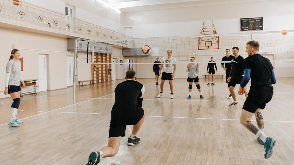 Eight adults play an energetic volleyball game, showcasing teamwork and athleticism on an indoor court.