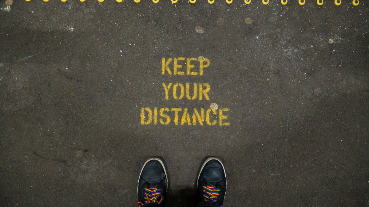 Social distancing sign on concrete floor in Edinburgh, Scotland, with rainbow shoelaced sneakers.
