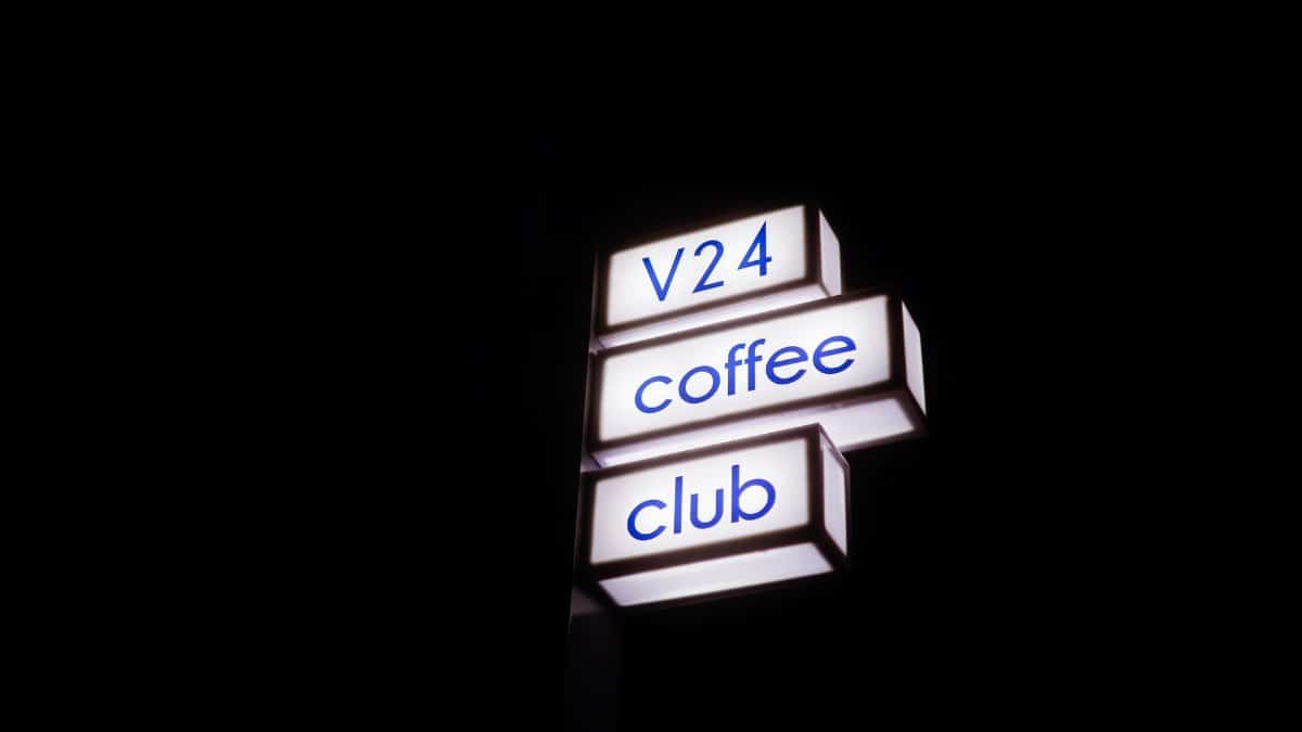 Brightly lit V24 Coffee Club sign with a dark night sky backdrop.